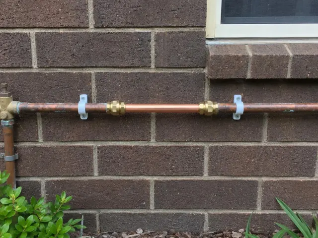 Repaired copper water pipe on a brick exterior wall under a window in Arcadia Vale
