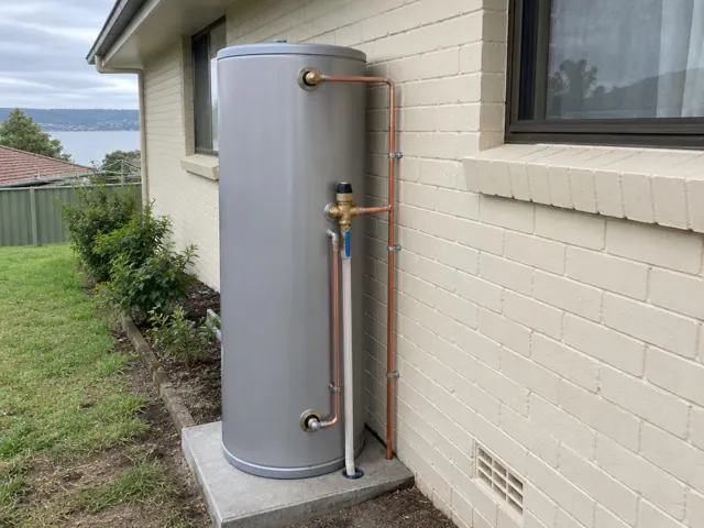 New hot water tank on a concrete slab beside a cream brick house with copper pipework in Wangi Wangi